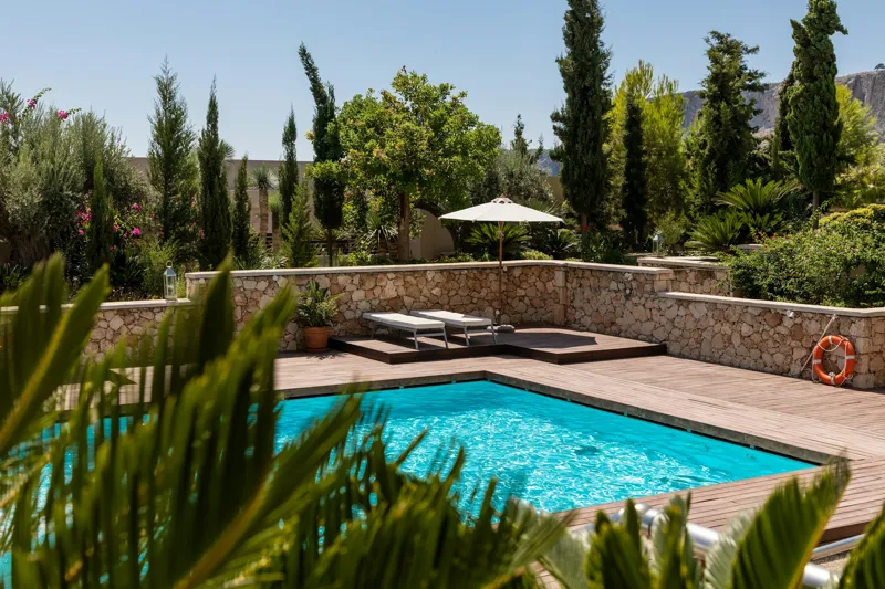 Sparkling clean turquoise backyard swimming pool surrounded by a sunny deck and garden
